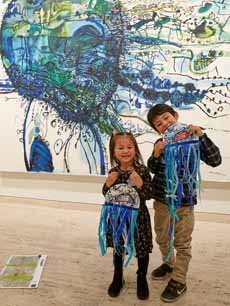 Two kids with art they have made in front of an artwork